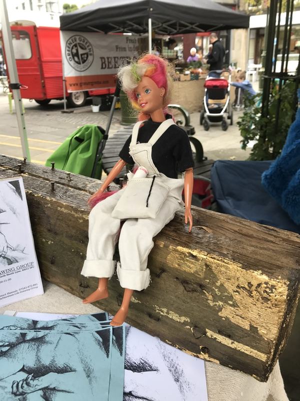 A doll in dungarees sitting on an old beam at a craft stall